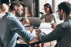 dure journée de travail. jeunes gens modernes en vêtements décontractés intelligents travaillant ensemble tout en étant assis dans le bureau de création photo