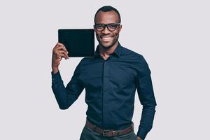copier l'espace sur sa tablette. beau jeune homme africain portant une tablette numérique sur son épaule et souriant en se tenant debout sur fond gris photo