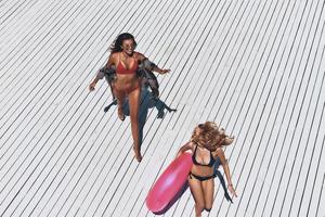 plaisir sous le soleil. vue de dessus de deux belles jeunes femmes en bikini souriant tout en courant à l'extérieur photo