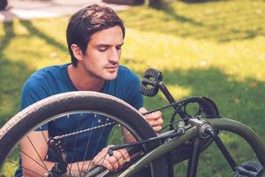 réparer son vélo. jeune homme confiant fixant son vélo tout en s'agenouillant sur l'herbe photo