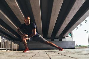 garder ces muscles flexibles. beau jeune homme africain en vêtements de sport qui s'étire tout en s'échauffant à l'extérieur photo