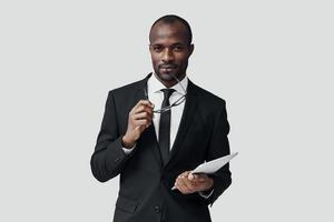 charmant jeune homme africain en tenues de soirée travaillant à l'aide d'une tablette numérique en se tenant debout sur fond gris photo