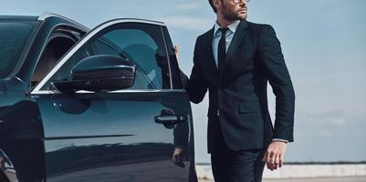 s'apprête à conduire. beau jeune homme d'affaires entrant dans sa voiture tout en se tenant à l'extérieur photo