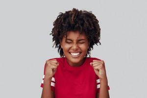 séduisante jeune femme africaine souriante et gesticulant en se tenant debout sur fond gris photo