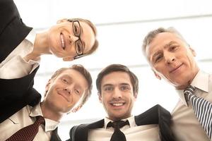 nous sommes une équipe commerciale solide. vue en angle bas de quatre hommes d'affaires joyeux debout près l'un de l'autre et souriant à la caméra photo