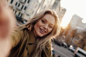 magnifique beauté. autoportrait d'une jeune femme attirante regardant la caméra et souriant tout en se tenant à l'extérieur photo