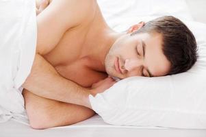 homme qui dort. beau jeune homme torse nu dormant en position couchée dans son lit photo