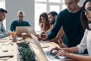 coopération dans l'action. groupe de jeunes gens modernes en vêtements décontractés intelligents utilisant des technologies modernes tout en travaillant dans le bureau de création photo