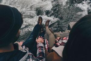 amoureux. vue de dessus en gros plan d'un jeune couple se tenant la main assis sur les rochers avec la rivière en contrebas photo