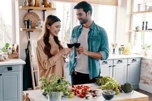 acclamations beau jeune couple préparant le dîner et buvant du vin debout dans la cuisine à la maison photo