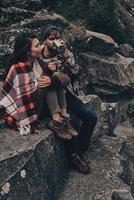 les voyages créent les meilleurs souvenirs. beau jeune couple recouvert d'une couverture se relaxant assis sur les rochers photo