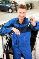 prends ta voiture. joyeux jeune homme en uniforme tendant la main avec des clés tout en se tenant près de la voiture à l'atelier photo