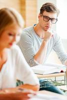 il ne manque jamais aucune conférence. jeune homme confiant tenant la main sur le menton et regardant la caméra assis à son bureau dans la salle de classe photo