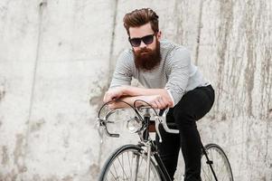 choisir les transports verts. beau jeune homme barbu appuyé sur son vélo tout en étant assis dessus contre le mur de béton photo