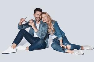 heureux de s'aimer. beau jeune couple regardant la caméra et souriant assis sur fond gris photo