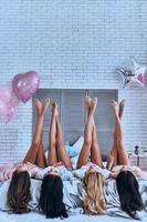 filles irrésistibles. jeunes femmes espiègles gardant les pieds en l'air allongées sur le lit avec des ballons partout dans la pièce photo