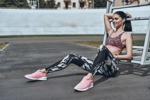 minute pour se reposer. belle jeune femme en tenue de sport souriante et regardant loin alors qu'elle était assise à l'extérieur photo