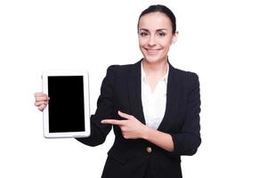 copier l'espace sur sa tablette. confiante jeune femme en tenues de soirée pointant sa tablette numérique et souriant tout en se tenant isolé sur blanc photo