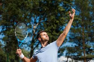 joueur de tennis servant la balle. vue en angle bas d'un joueur de tennis masculin confiant servant une balle photo