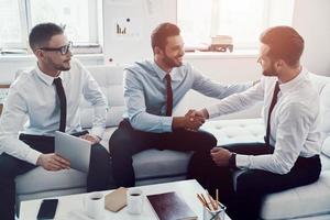 jeunes hommes modernes en tenues de soirée se serrant la main tout en travaillant au bureau photo