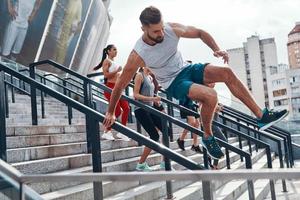 jeune homme en vêtements de sport sautant tout en faisant de l'exercice avec ses amis dans les escaliers à l'extérieur photo