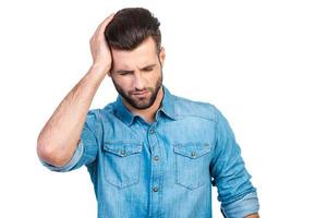 sensation de mal de tête. frustré jeune bel homme en chemise jeans touchant sa tête avec la main et gardant les yeux fermés en se tenant debout sur fond blanc photo