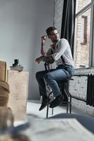 a quelque chose en tête. beau jeune homme regardant par la fenêtre par-dessus son épaule alors qu'il était assis sur un tabouret photo