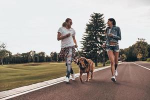 heureux d'être amoureux. toute la longueur d'un beau jeune couple courant avec son chien tout en passant du temps à l'extérieur photo