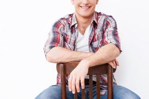 confiant et créatif. gros plan d'un beau jeune homme souriant assis sur la chaise et sur fond blanc photo