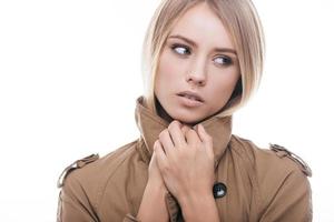 à l'aise dans son nouveau manteau. séduisante jeune femme en manteau couvrant son cou avec un col et regardant loin en se tenant debout sur fond blanc photo