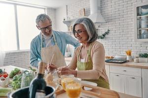 couple de personnes âgées actif en tablier préparant un dîner sain et souriant tout en passant du temps à la maison photo