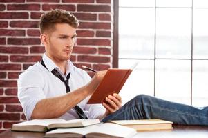 il a un esprit créatif. beau jeune homme en chemise et cravate écrivant quelque chose dans un bloc-notes assis sur son lieu de travail photo