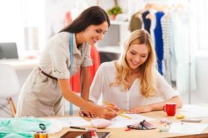 créer leurs nouveaux modèles. deux jeunes femmes heureuses travaillant ensemble dans leur atelier de mode photo