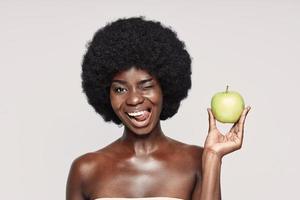 portrait d'une belle jeune femme africaine tenant une pomme verte et un clin d'œil photo