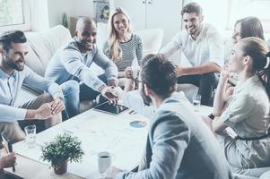 bienvenue à bord d'un groupe de gens d'affaires confiants assis autour du bureau ensemble pendant que deux hommes se serrent la main et sourient photo