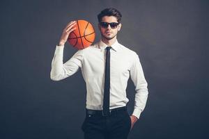 jouer selon ses propres règles. beau jeune homme en chemise et cravate tenant un ballon de basket sur son épaule et regardant la caméra en se tenant debout sur fond gris photo