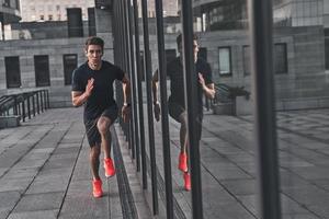 continuer à courir. toute la longueur du jeune homme en vêtements de sport courant tout en faisant de l'exercice à l'extérieur photo