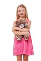 petite fille avec ours en peluche. joyeuse petite fille en robe rose tenant un ours en peluche et regardant la caméra tout en étant isolée sur blanc photo