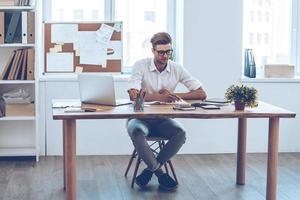 prendre quelques notes. pensif jeune bel homme écrivant dans son cahier tout en étant assis sur son lieu de travail photo