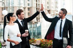 célébrer le succès. deux jeunes hommes d'affaires heureux donnant un high five tandis que leur collègue tenant une tablette numérique et souriant photo