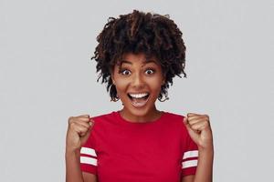 séduisante jeune femme africaine regardant la caméra avec le sourire et gesticulant en se tenant debout sur fond gris photo