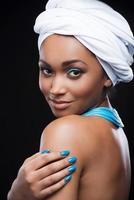 belles femmes africaines. belle femme africaine portant un foulard et touchant sa peau tout en regardant la caméra et debout sur fond noir photo