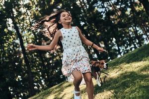 se sentir libre et heureux. jolie petite fille souriante en courant avec son chien à l'extérieur photo