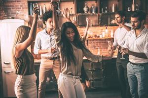 profiter d'une fête à la maison cool. jeunes joyeux dansant et buvant tout en profitant d'une fête à la maison dans la cuisine photo