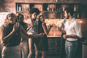 danse insouciante avec des amis. jeunes joyeux dansant et buvant tout en profitant d'une fête à la maison dans la cuisine photo