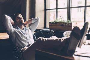 le temps de se détendre. beau jeune homme dormant sur son lieu de travail au bureau tout en se tenant les mains derrière la tête photo