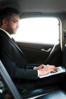 homme d'affaires en déplacement. jeune homme d'affaires confiant travaillant sur un ordinateur portable tout en étant assis dans sa voiture photo