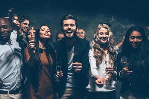 célébrer avec plaisir. groupe de jeunes joyeux portant des cierges magiques et des flûtes à champagne photo