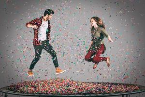 plaisir en l'air. tir en l'air d'un beau jeune couple joyeux sautant sur un trampoline avec des confettis tout autour d'eux photo