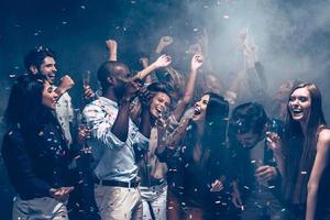 plaisir insouciant. groupe de beaux jeunes lançant des confettis colorés et ayant l'air heureux photo